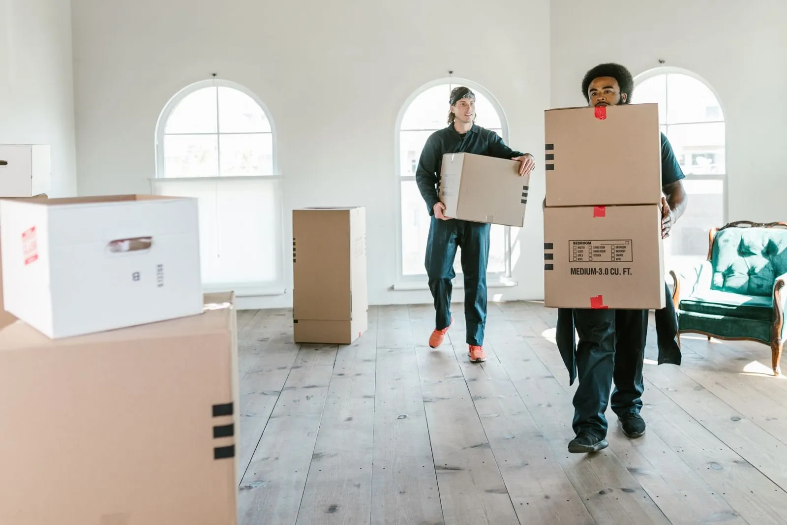 Two Urban Relocations movers carrying packed cartons into a new home